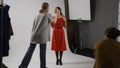 Backstage of model and professional team in the studio. Female assistant fixes makeup for model in red dress Royalty Free Stock Photo