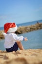 Backview of child in Santa hat sitting on seashore