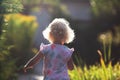 Backview of happy cheerful small girl with blond curly hair running in the garden in sunny summer day
