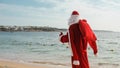 Photo of Santa Claus with Christmas sack full of gifts walking on the beach Royalty Free Stock Photo