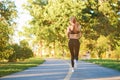 Backview of sporty girl running along racetrack in the city park.