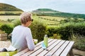 Backview young man sitting behind a wooden table and enjoying beautiful local nature view with tea thermos and