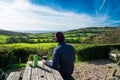 Backview young man in warm clothes sitting in farmer wooden cafe and enjoying local nature view with tea thermos on