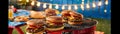 Backyard BBQ setup with beef burgers cooking on the grill, picnic table, and string lights, evening barbecue Royalty Free Stock Photo