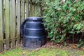 Backyard composter next to a fence and hedge Royalty Free Stock Photo