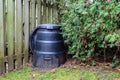 Backyard composter next to a fence and hedge Royalty Free Stock Photo