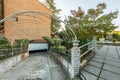 Backyard of a villa with a ramp leading down to a garage with a white metal gate and a paved walkway between hedges and pots