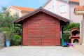 Backyard wooden storage structure with stone tiles in front surrounded with plants and stone wall with houses and clear blue sky