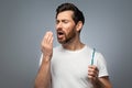 Bad breath. Handsome middle aged man checking his breath with his hand, blowing to it, standing over grey background Royalty Free Stock Photo