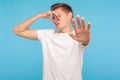 Bad breath. Portrait of confused man in casual white t-shirt pinching nose and showing stop gesture