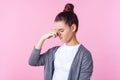 Bad breath, stink. Portrait of brunette teenage girl standing with closed eyes and pinched nose. isolated on pink background