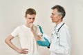 Bad news. Mature professional doctor in medical uniform and blue sterile gloves speaking with worried young male patient Royalty Free Stock Photo