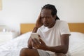 Bad News. Stressed Black Guy Sitting On Bed And Looking At Smartphone Royalty Free Stock Photo