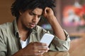 Bad News. Upset Black Guy Looking At Smartphone While Sitting At Cafe Royalty Free Stock Photo