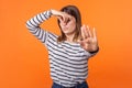 Bad smell. Portrait of young woman with brown hair in long sleeve striped shirt. indoor studio shot isolated on orange background