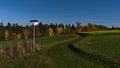 Beautiful view of signpost aside hiking trail leading over green meadow with colorful trees rapeseed.