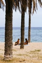 Badalona, Spain - August 10, 2020. Two young women on the beach under palm trees. Social distancing concept