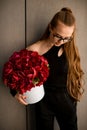 Baeutiful view of young attractive brunette girl with big round box of red peony flowers standing near wall Royalty Free Stock Photo