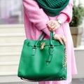 Bag close-up in female hands. Stylish modern and feminine image, style. Girl with a green bag in a pink coat Royalty Free Stock Photo