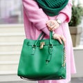 Bag in female hands. Bright leather bag. accessories. Pink coat and green bag.