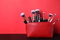 Bag with makeup brushes and cosmetic products on black table against red background. Space for text Royalty Free Stock Photo