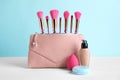 Bag with makeup brushes and cosmetic products on white table against light blue background Royalty Free Stock Photo