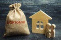 A bag with money and the word Mortgage and a wooden house. The accumulation of money to pay interest rates on mortgages. Buying a Royalty Free Stock Photo