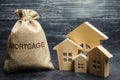 A bag with money and the word Mortgage and a wooden houses. The accumulation of money to pay interest rates on mortgages. Buying a Royalty Free Stock Photo