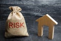 A bag with money and the word risk and a wooden house. Buying property on credit. The concept of financial risk. Loss of housing