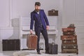 Baggage delivery concept. Macho elegant on strict face stands near pile of vintage suitcase, holds suitcase. Man