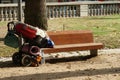 Baggage trolley with sleeping bag and hand luggage of a homeless person leaned against wooden bench. Royalty Free Stock Photo