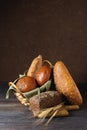A baguette, pumpkin bread, a loaf of rye bread and two buns in a wicker basket on a dark wooden background. Bread still life Royalty Free Stock Photo