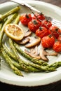 Baked asparagus and cherry tomatoes in a plate, close-up