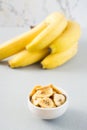 Baked banana chips in a white bowl and a bunch of bananas on the table. Fast food. Close-up. Vertical view Royalty Free Stock Photo