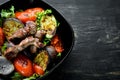 Baked beef and grilled vegetables in a black plate. On a wooden background.