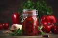 Baked canned red paprika pepper, marinated with chili, garlic and herbs in glass jar. Rustic wood kitchen table background