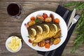 Baked carp with vegetables grilled on a white plate and a glass of red wine on a wooden background Royalty Free Stock Photo