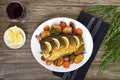 Baked carp with vegetables grilled on a white plate and a glass of red wine on a wooden background. Royalty Free Stock Photo