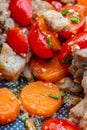 Baked carrot pieces, cherry tomatoes, garlic with small pieces of meat. Green onions. Shallow depth of field.