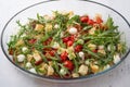 Baked cherry tomatoes, rucola, croutons, red onion, garlic, spices and cheese in a glass baking dish on a light gray
