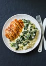 Baked chicken breast, mashed potatoes with creamy spinach on dark background, top view