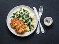 Baked chicken breast, mashed potatoes with creamy spinach on dark background, top view.