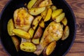 Baked chicken drumsticks with potatoes in cast-iron frying pan on wooden table. Top view Royalty Free Stock Photo