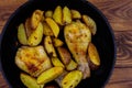Baked chicken drumsticks with potatoes in cast-iron frying pan on wooden table. Top view Royalty Free Stock Photo