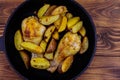 Baked chicken drumsticks with potatoes in in cast-iron frying pan on wooden table. Top view Royalty Free Stock Photo