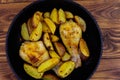 Baked chicken drumsticks with potatoes in in cast-iron frying pan on wooden table. Top view Royalty Free Stock Photo