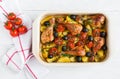 Baked chicken drumsticks in red dish. Cooked with cherry tomatoes, black olives, rosemary and potatoes. White wooden table Royalty Free Stock Photo