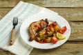 Baked chicken leg with potatoes and tomato on a white plate with a fork on a wooden table. Royalty Free Stock Photo