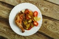 Baked chicken leg with potatoes and tomato on a white plate on a wooden table. Royalty Free Stock Photo