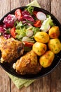 Baked chicken thighs with a garnish of new potatoes and fresh salad close-up on a plate. Vertical top view Royalty Free Stock Photo